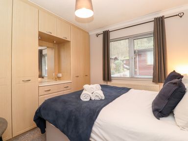 A bedroom with a bed with folded towels on a blanket and built in wardrobes next to a window at Hill Lodge Applethwaite 2 Limefitt Park near Windermere