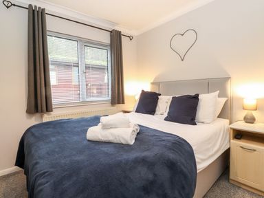 A bedroom with a bed with blue bedding and pillows beside a window with gray curtains at Hill Lodge in Applethwaite 2 Limefitt Park near Windermere