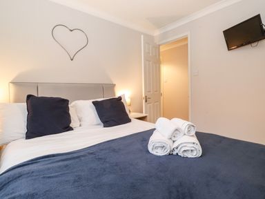 A bedroom with a bed with white and navy bedding white rolled towels on the bed a heart-shaped wall decoration and a wall-mounted TV at Hill Lodge Applethwaite 2 Limefitt Park near Windermere
