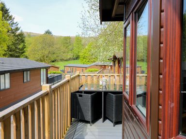 A balcony with a glass table and black chairs overlooking other similar wooden lodges at Hill Lodge in Applethwaite 2 Limefitt Park near Windermere