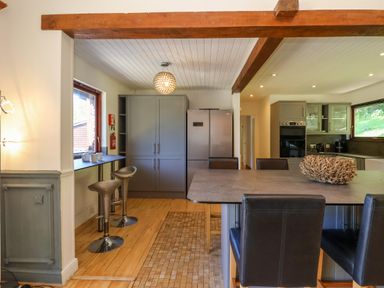 A kitchen with bar stools by a window grey cabinets and an island with chairs at Bay Tree Lodge 35 Watermouth near Berrynarbor