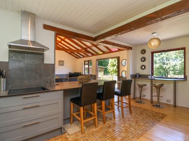 A kitchen with bar stools along a counter and a window with trees outside at Bay Tree Lodge 35 Watermouth near Berrynarbor