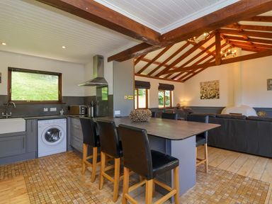 An open plan kitchen and living area with an island and chairs and exposed wooden beams at Bay Tree Lodge 35 Watermouth near Berrynarbor