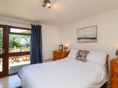 A bedroom with a double bed two wooden bedside tables lamps a window with curtains and a door leading outside at Bay Tree Lodge 35 Watermouth near Berrynarbor
