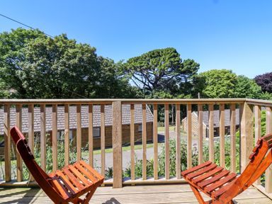 A balcony with wooden chairs and railing overlooking trees and buildings at Bay Tree Lodge 35 in Watermouth near Berrynarbor