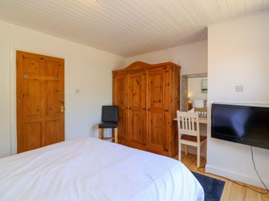 A bedroom with a wooden wardrobe a chair a wall-mounted tv and a small white desk with a mirror at Bay Tree Lodge 35 Watermouth near Berrynarbor