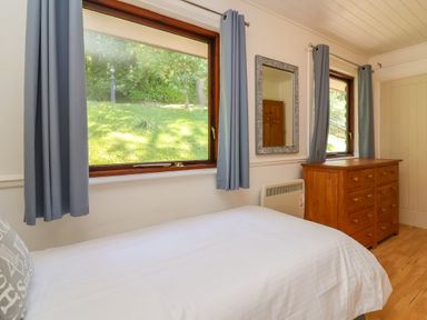 A bedroom with a bed a wooden dresser two windows with curtains and a wall mirror at Bay Tree Lodge 35 Watermouth near Berrynarbor