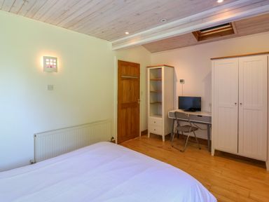 A bedroom with a bed a wooden door a white wardrobe a desk with a monitor and a chair at Bay Tree Lodge 35 Watermouth near Berrynarbor