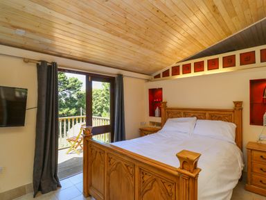 A bedroom with a wooden bed and bedside tables and a door leading to a balcony at Bay Tree Lodge 35 Watermouth near Berrynarbor