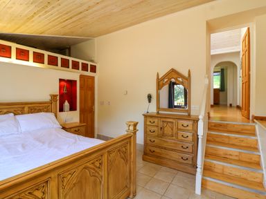 A bedroom with a wooden bed a wooden dresser with a mirror and stairs leading to another room at Bay Tree Lodge 35 Watermouth near Berrynarbor