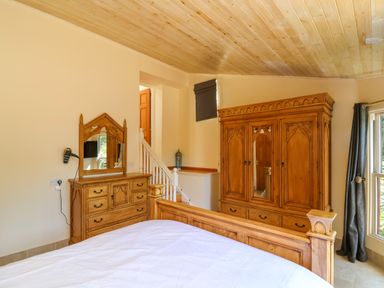 A bedroom with wooden furniture a bed a dresser with a mirror a wardrobe and a window with curtains at Bay Tree Lodge 35 Watermouth near Berrynarbor