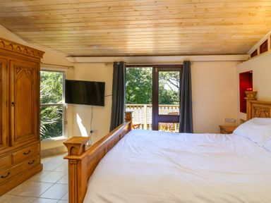 A bedroom with a wooden bed and wardrobe a wall-mounted tv and a door leading to a balcony at Bay Tree Lodge 35 Watermouth near Berrynarbor