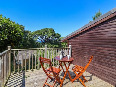 A wooden balcony with two chairs and a table with mugs and a lantern at Bay Tree Lodge 35 Watermouth near Berrynarbor