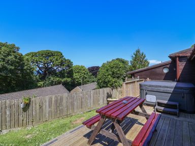 An outdoor deck with a picnic table and hot tub overlooking trees and rooftops at Bay Tree Lodge 35 in Watermouth near Berrynarbor