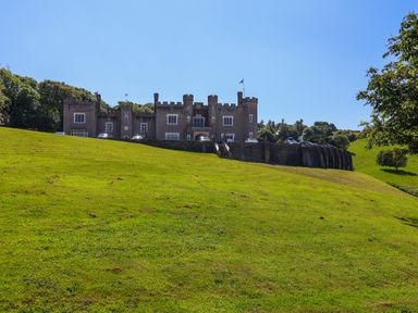 A large castle on a hill with a green grassy foreground and cars parked in front at Bay Tree Lodge 35 Watermouth near Berrynarbor