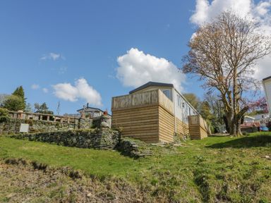 An elevated mobile home with wooden fencing and stone retaining walls on a grassy slope with a tree nearby at 11A Mansion View in Cove near Kilcreggan