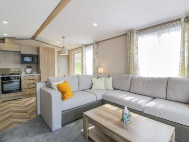 A living room with a grey sectional sofa and wooden coffee table next to an open kitchen area at 11A Mansion View in Cove near Kilcreggan