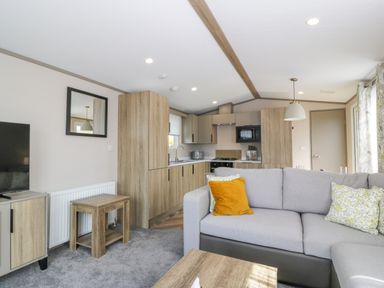 A living room with a grey sofa with cushions a wooden coffee table a TV and a kitchen with wooden cabinets at 11A Mansion View in Cove near Kilcreggan