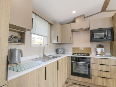 A kitchen with cabinets a sink a kettle a toaster a microwave an oven a gas stove and a knife set at 11A Mansion View in Cove near Kilcreggan