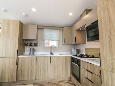 A kitchen with wood cabinets a sink a kettle a toaster a gas stove an oven and a microwave at 11A Mansion View in Cove near Kilcreggan