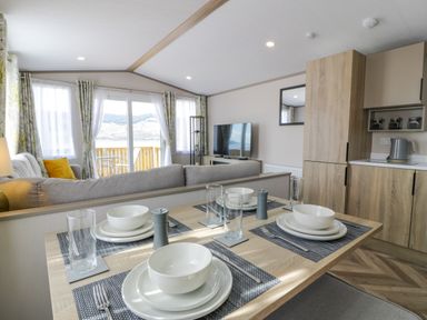 A dining table set for four in an open living space with a sofa television and kitchen area at 11A Mansion View in Cove near Kilcreggan