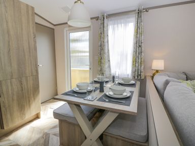 A dining area with a table set for four with bowls plates glasses and cutlery near a window with curtains and a sofa at 11A Mansion View in Cove near Kilcreggan
