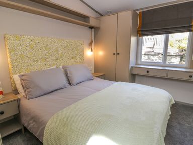 A bedroom with a bed two bedside tables a wardrobe a window with a blind and a shelf above the bed at 11A Mansion View Cove near Kilcreggan