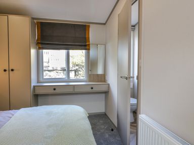 A bedroom with a bed wardrobe drawers a window and an open door leading to a bathroom at 11A Mansion View in Cove near Kilcreggan