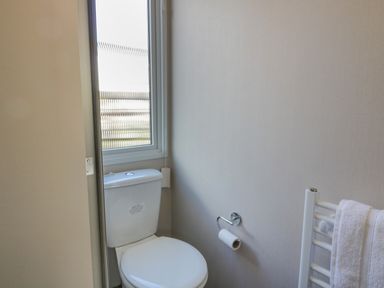 A bathroom with a toilet a window a toilet paper holder and a towel rack at 11A Mansion View in Cove near Kilcreggan