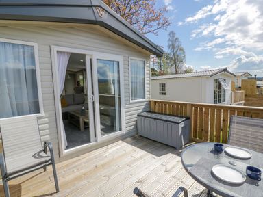 An outdoor wooden deck with chairs and a glass table set with plates and cups outside a mobile home at 11A Mansion View in Cove near Kilcreggan
