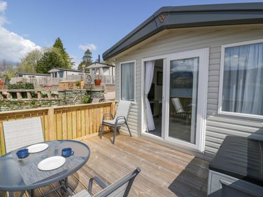 A wooden deck with a glass table set with plates and cups and chairs outside a house at 11A Mansion View in Cove near Kilcreggan