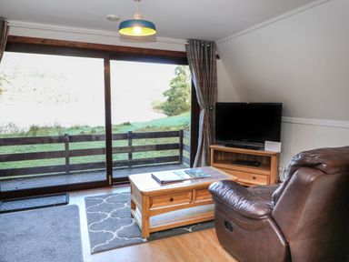 A living room with a leather armchair wooden coffee table television and large sliding glass doors at 27 Invergarry Lodges South Laggan near Invergarry