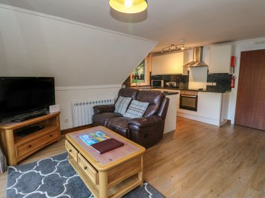 A living room with a leather sofa a wooden coffee table a television and an open kitchen at 27 Invergarry Lodges South Laggan near Invergarry