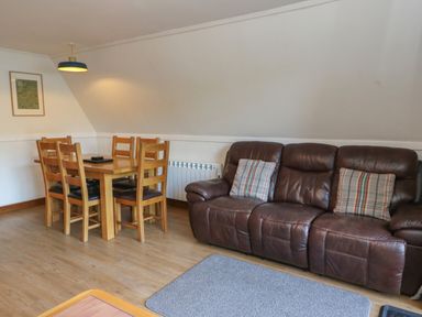 A dining table with six wooden chairs and a brown leather sofa with cushions in a living room at 27 Invergarry Lodges South Laggan near Invergarry