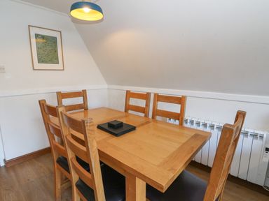 A dining room with a wooden table and six chairs under a hanging light at 27 Invergarry Lodges in South Laggan near Invergarry