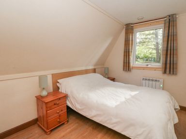 A bedroom with a bed and two wooden bedside tables with lamps next to a window with curtains at 27 Invergarry Lodges in South Laggan near Invergarry