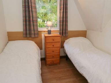 A bedroom with two single beds separated by a wooden chest of drawers with a lamp on top at 27 Invergarry Lodges South Laggan near Invergarry
