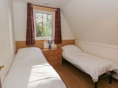 A bedroom with two single beds a wooden chest of drawers and a window with red plaid curtains at 27 Invergarry Lodges in South Laggan near Invergarry
