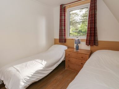A bedroom with two single beds a wooden bedside cabinet with a lamp and a window with red plaid curtains at 27 Invergarry Lodges South Laggan near Invergarry