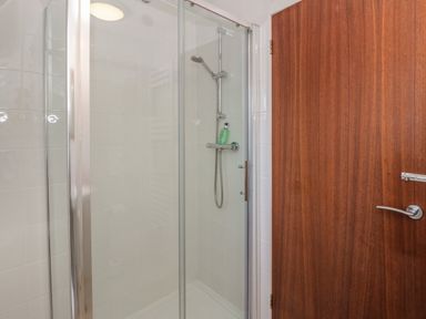 A shower enclosure with a glass door and a showerhead inside and a wooden door next to it at 27 Invergarry Lodges in South Laggan near Invergarry