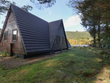 A wooden lodge with a steep roof near grassy land and trees at 27 Invergarry Lodges in South Laggan near Invergarry