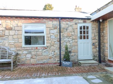 A stone exterior wall with a window and a white door and a wooden bench at Wellington Lodge Cottage in Middleton Tyas