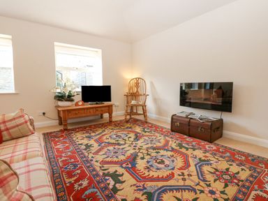 A living room with a patterned rug sofa table with a TV and flowers wooden chair and wall-mounted television at Wellington Lodge Cottage in Middleton Tyas