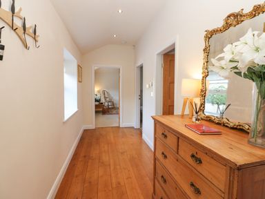 A hallway with wooden floor a wooden dresser with a mirror a lamp and flowers in a vase at Wellington Lodge Cottage in Middleton Tyas