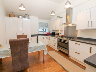 A kitchen with white cabinets a wooden floor a dining table with chairs and stainless steel appliances at Wellington Lodge Cottage Middleton Tyas