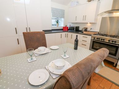 A kitchen with a dining table set with plates bowls glasses and a bottle next to white cabinets and a stove at Wellington Lodge Cottage in Middleton Tyas