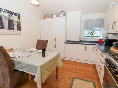A kitchen with white cabinets wooden floor a dining table with chairs and tableware at Wellington Lodge Cottage in Middleton Tyas
