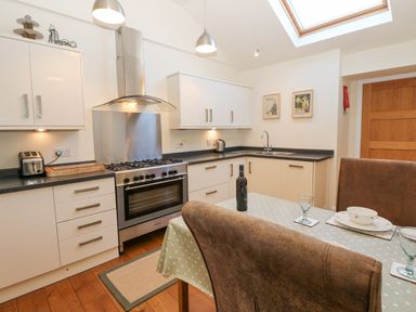 A kitchen with white cabinets a stainless steel stove black countertops and a dining table with chairs at Wellington Lodge Cottage in Middleton Tyas