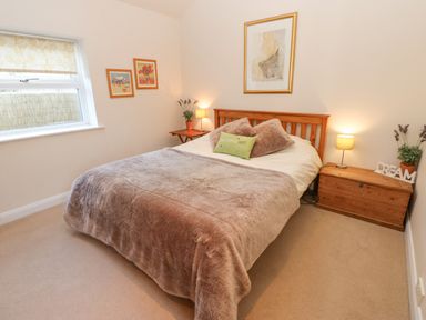 A bedroom with a wooden bed a brown blanket two side tables with lamps and framed pictures on the walls at Wellington Lodge Cottage in Middleton Tyas