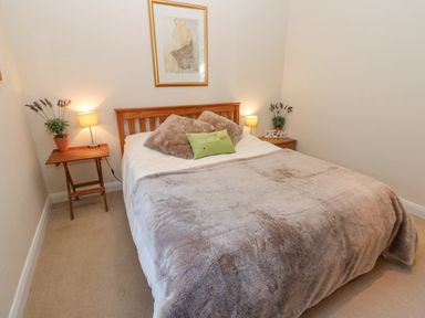 A bedroom with a double bed two bedside tables with lamps and plants and a framed picture on the wall at Wellington Lodge Cottage in Middleton Tyas